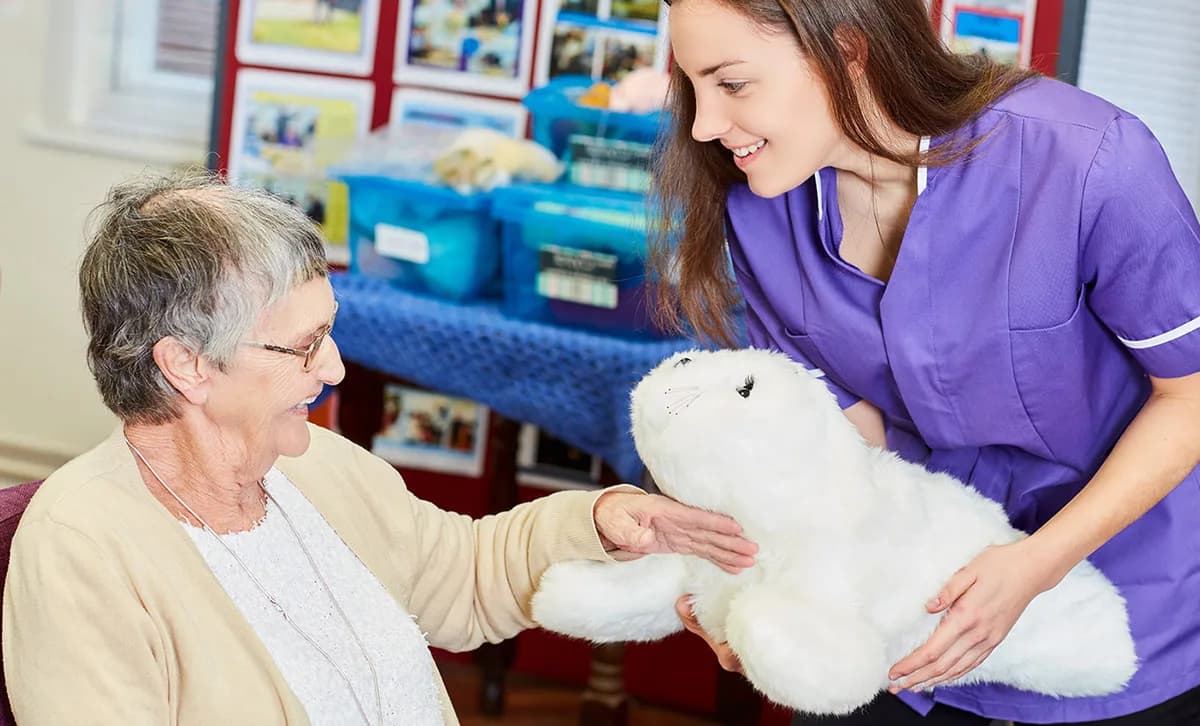 A care worker introduces the PARO robot seal to an older woman