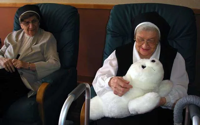 An older man holding the PARO robot seal in a care home